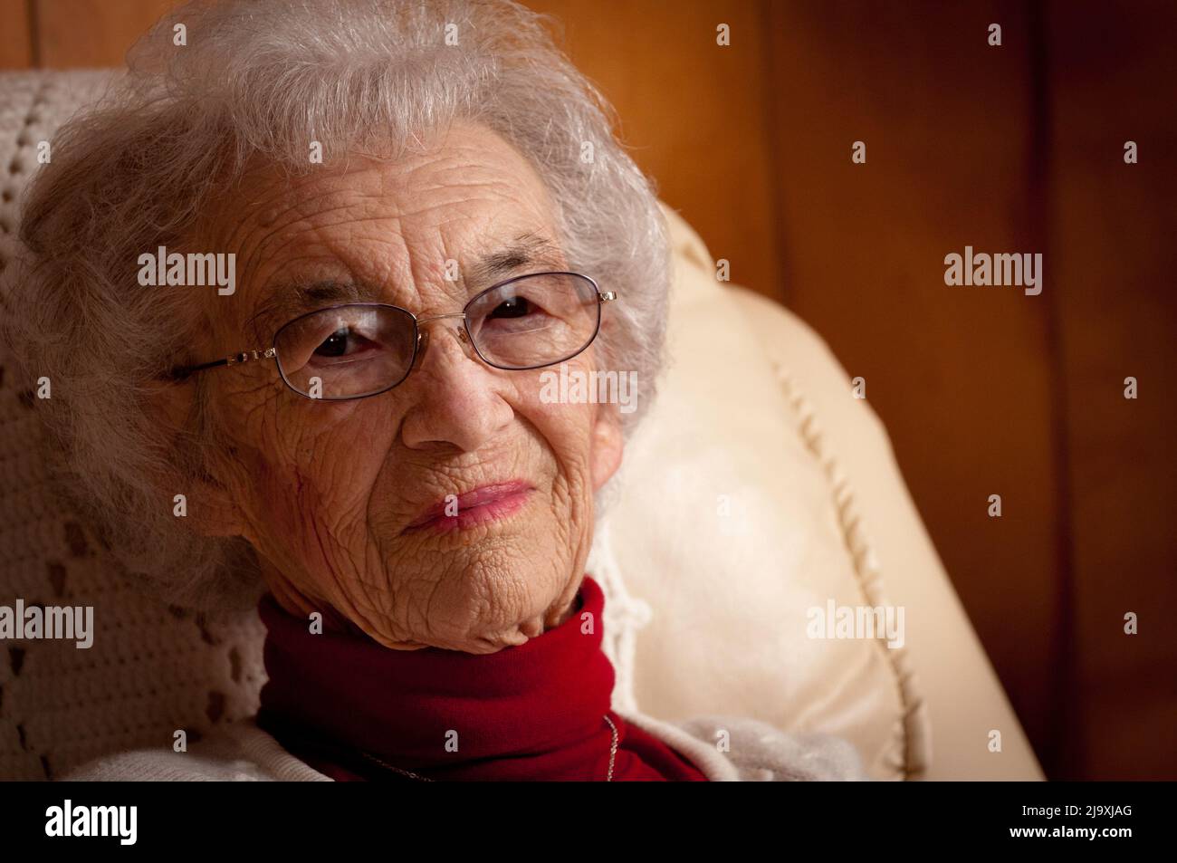 Portrait of an elderly woman sitting on a chair and looking at the camera Stock Photo