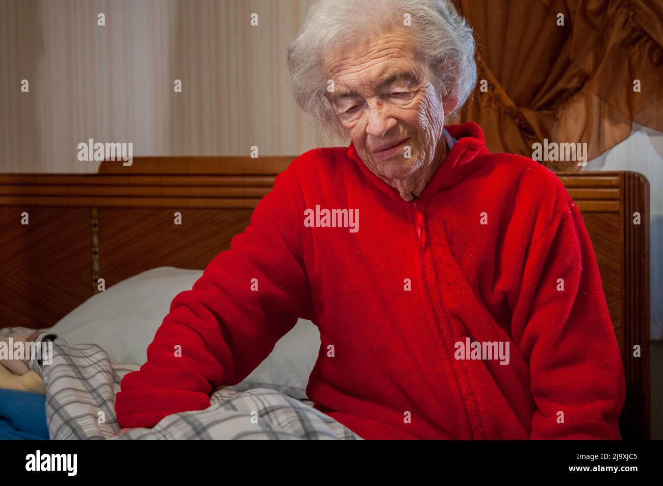 Elderly woman in bathrobe getting up out of bed in the morning Stock Photo