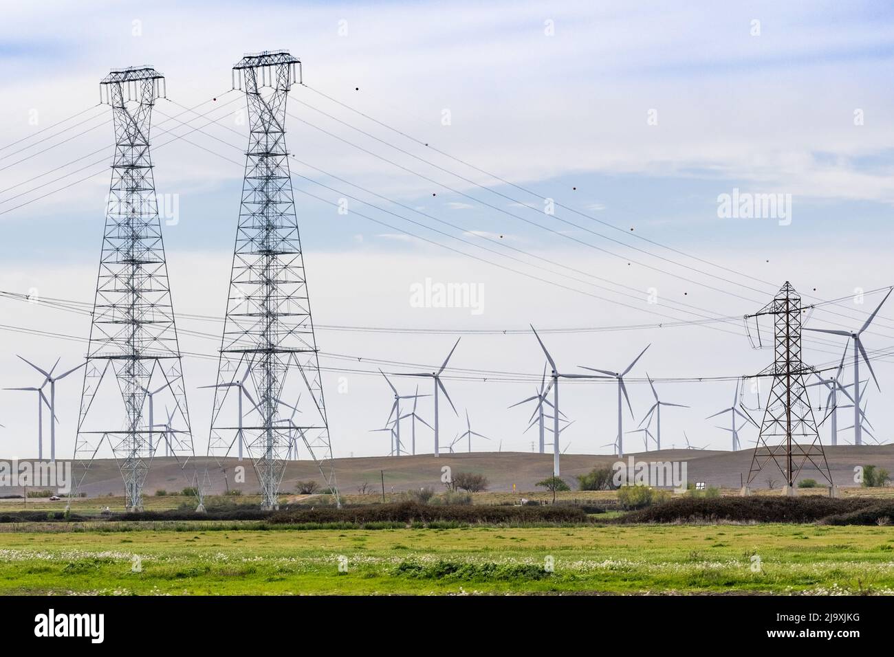 High voltage electricity towers and lines crossing the Sacramento-San Joaquin Delta; Wind turbines visible on the hills in the background; Solano Coun Stock Photo