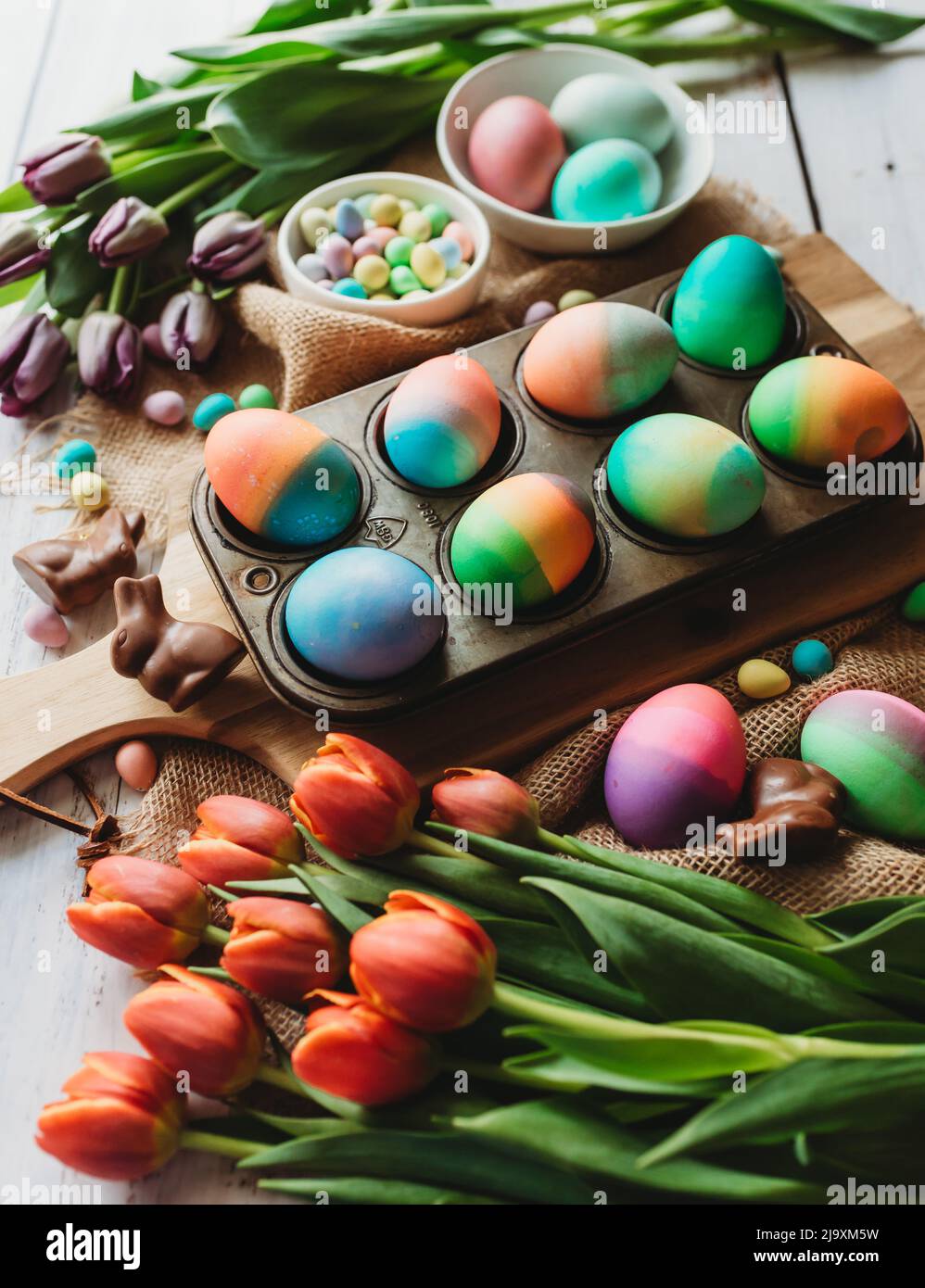 Tray of brightly colored easter eggs surrounded by tulips. Stock Photo