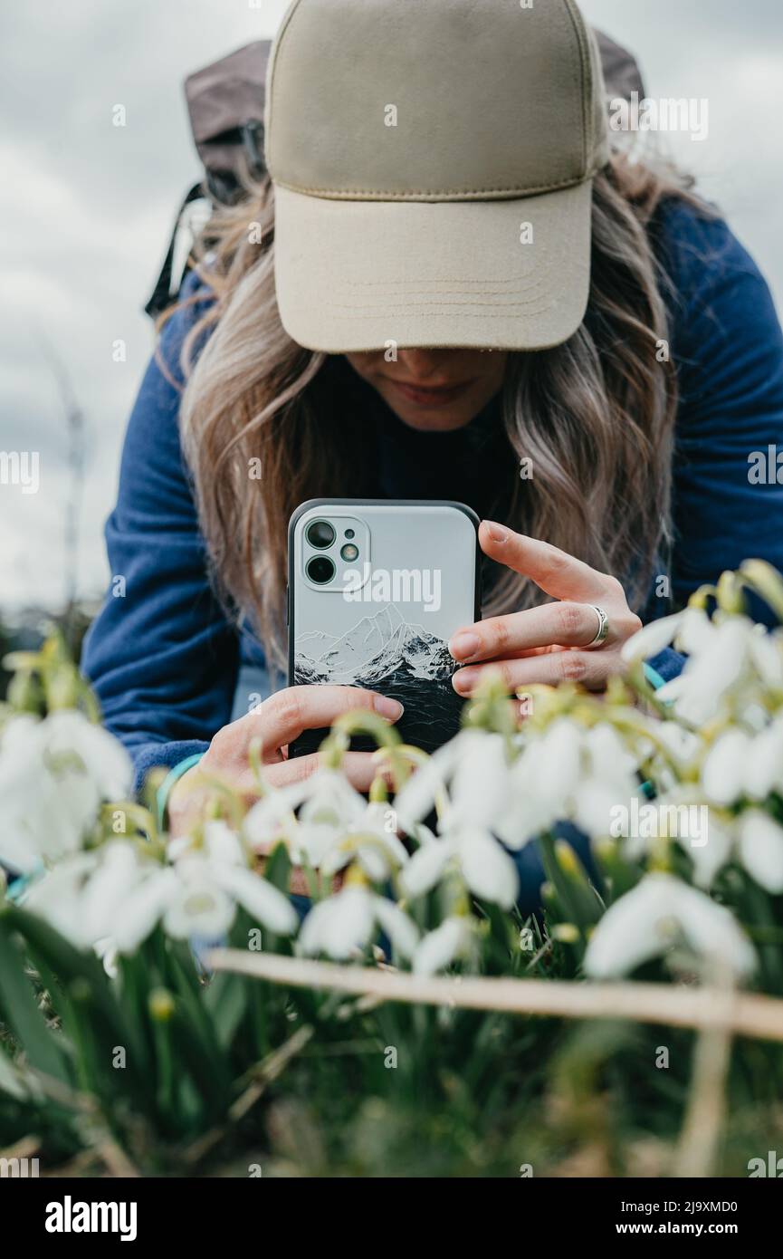 Young girl with hat taking take pictures of flowers with phone Stock