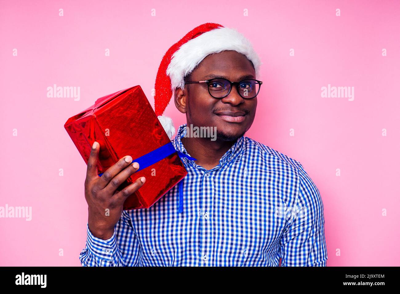 African American man wearing stylish plaid shirt great smile in santa hat with gift box on pink background studio.dark-skinned Santa Claus Stock Photo
