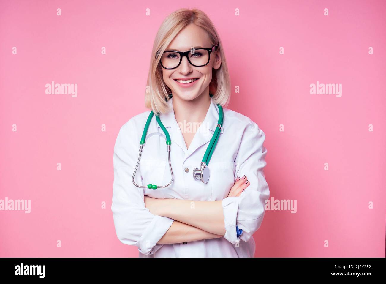 Portrait of a smiling female gynecologist doctor.beautiful blonde woman in white medical coat and glasses holding a stethoscope on a pink background Stock Photo