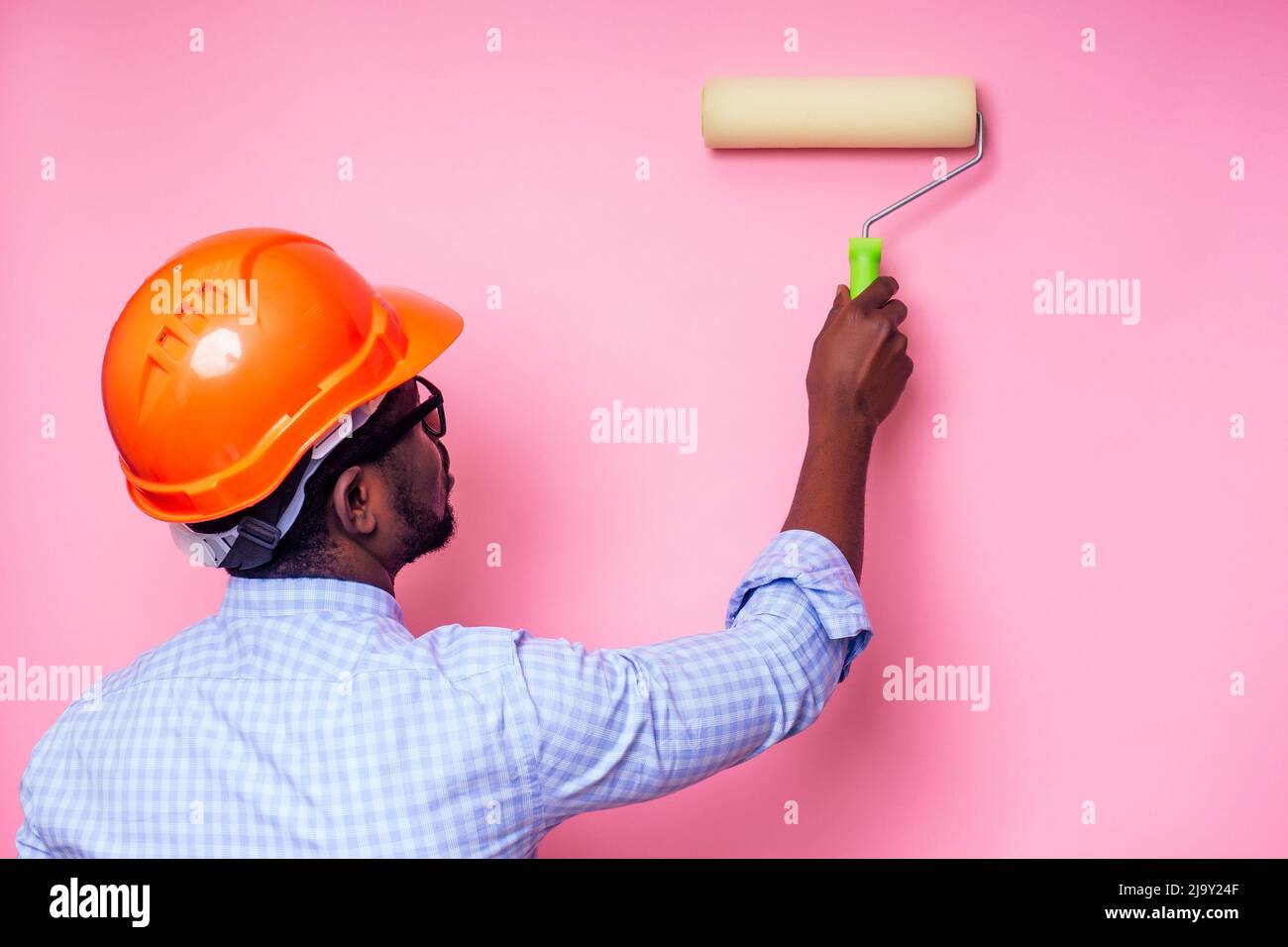 black man African American holding paint roller in hand paints the wall in pink color .happy african builder painting inside the house,businessman Stock Photo