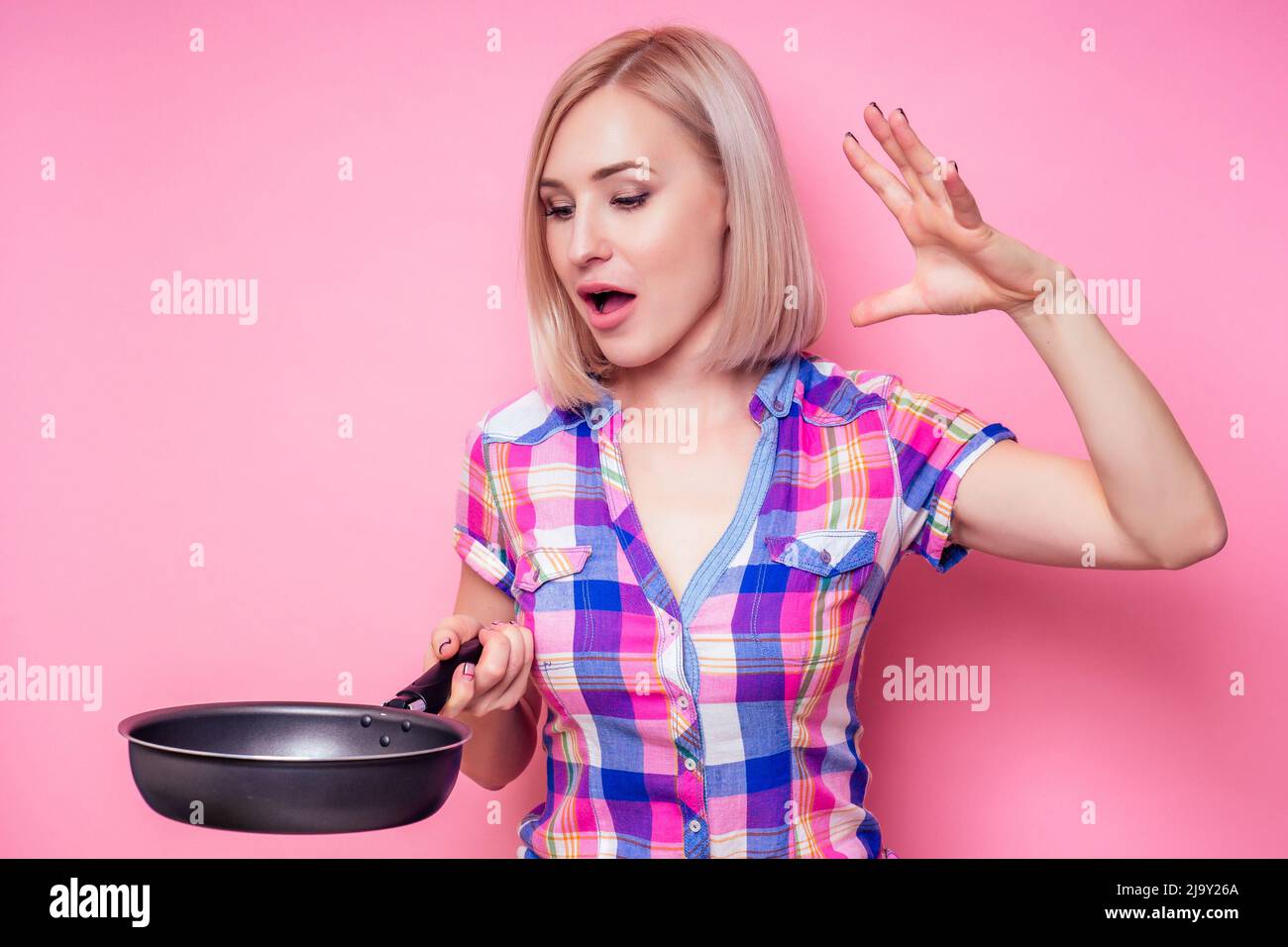 Beautiful blonde housewife woman holding pan on a pink background in the studio Stock Photo