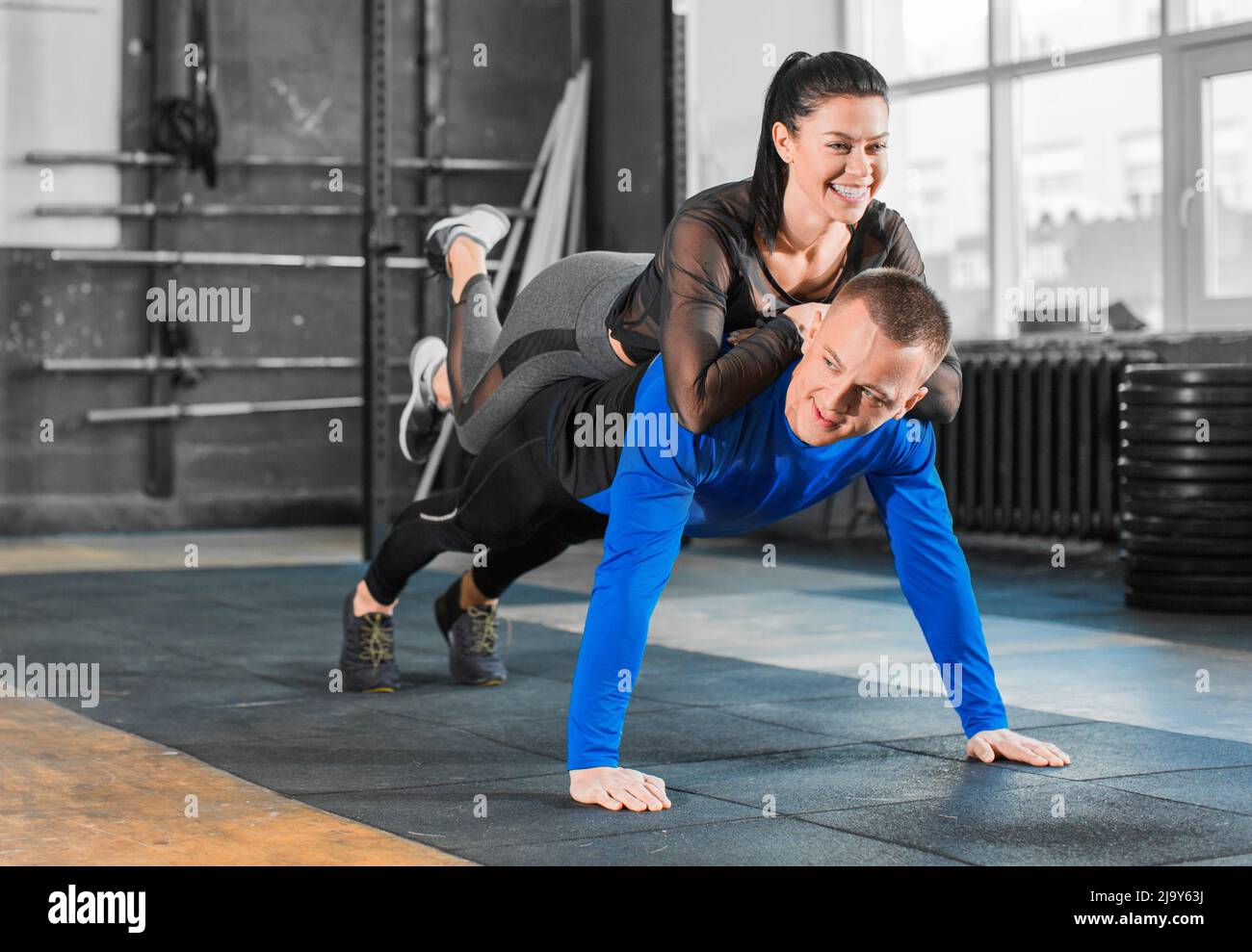 Push-ups with woman on back. Healthy couple in gym, workout with own body weight. Active and sporty lifestyle concept Stock Photo