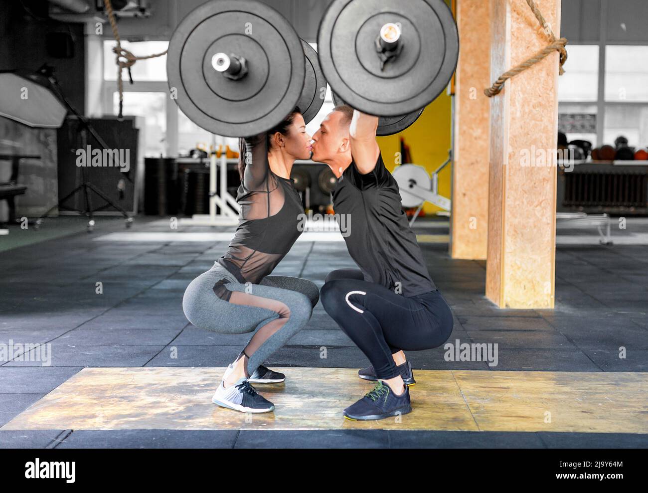 Fitness couple making a Barbell Jerk and kissing each other. Sporty family in gym. Side view. Stock Photo