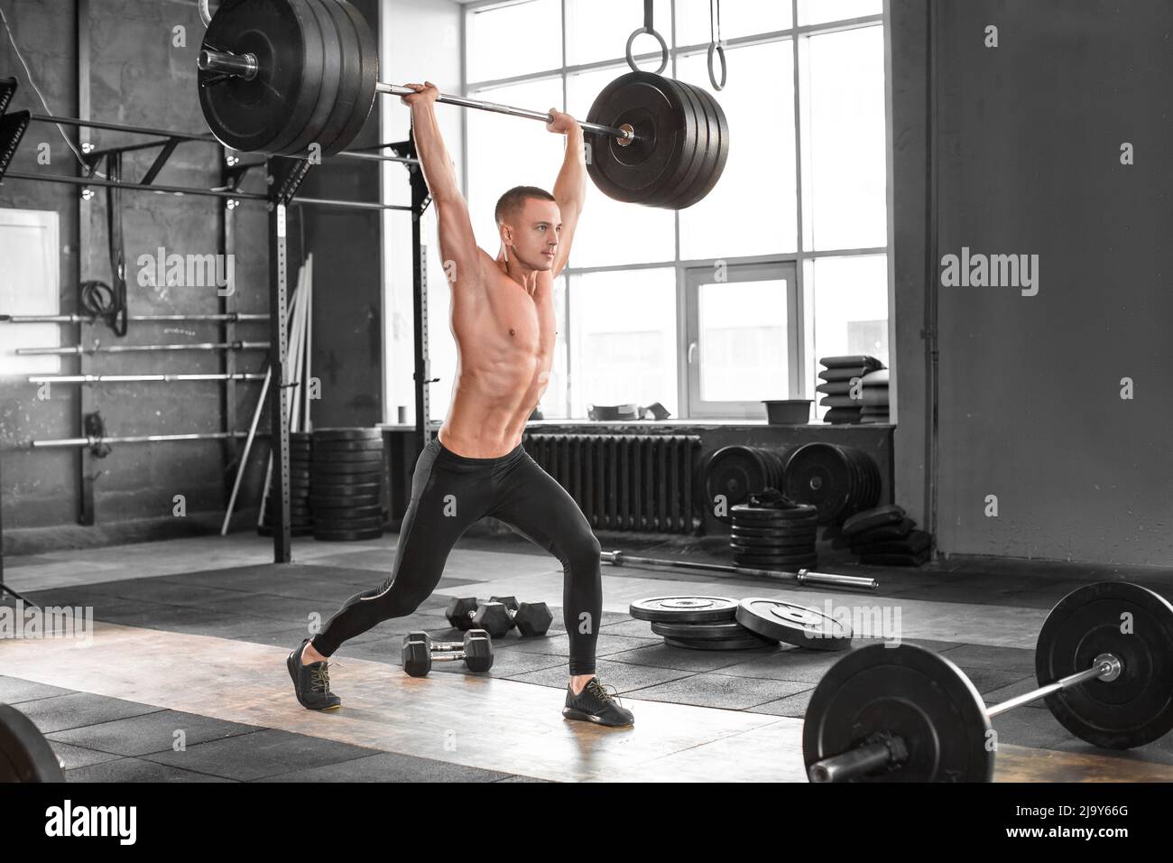Man train with heavy barbell raised over head with a bar in gym