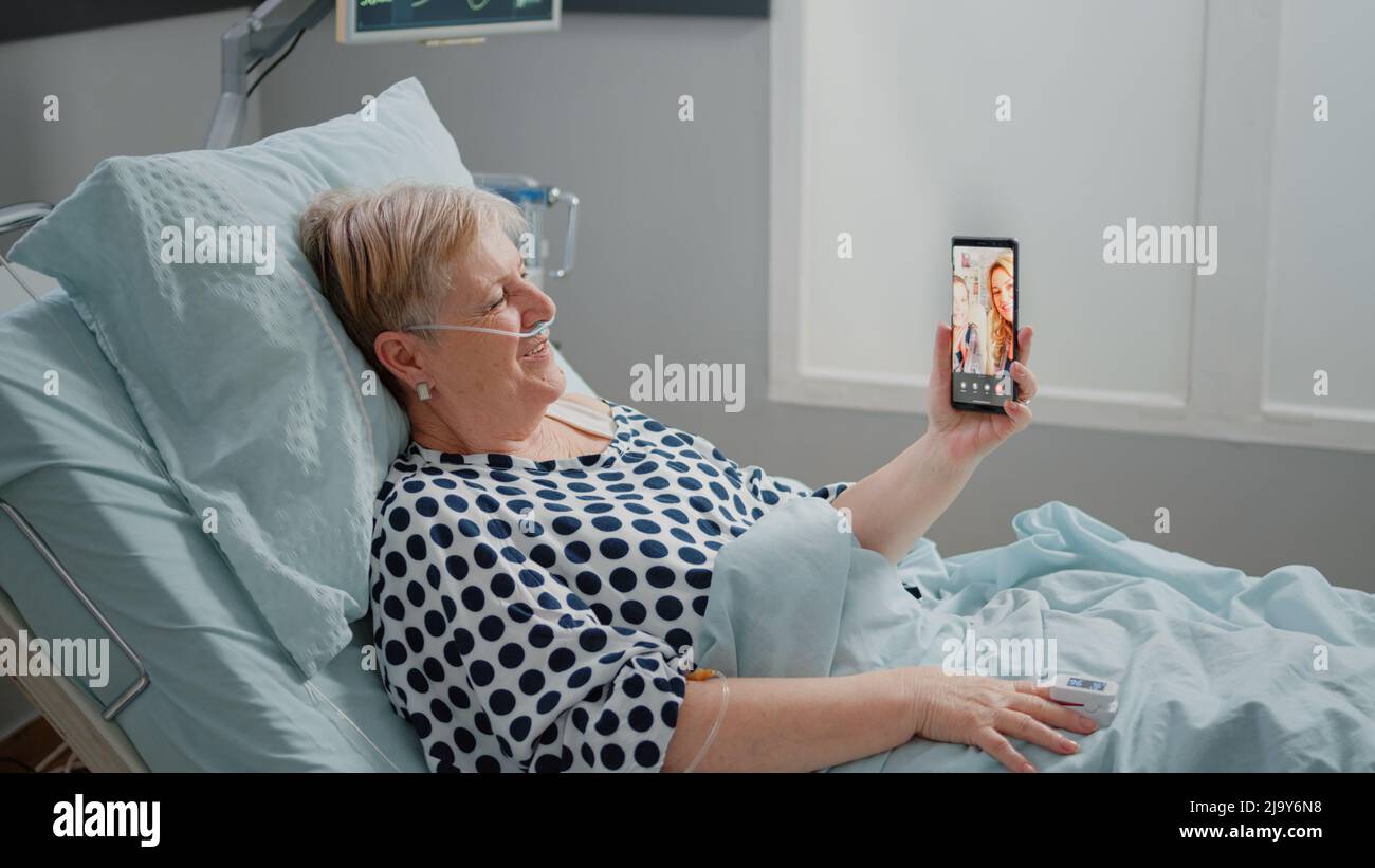 Senior patient talking to family on video call in hospital ward bed