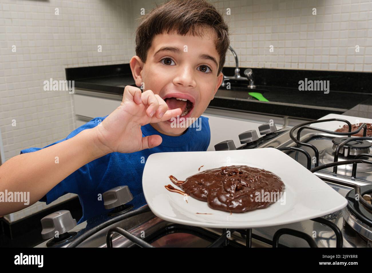 8 year old child in front of a plate of sweet brigadeiro and licking his finger. Stock Photo