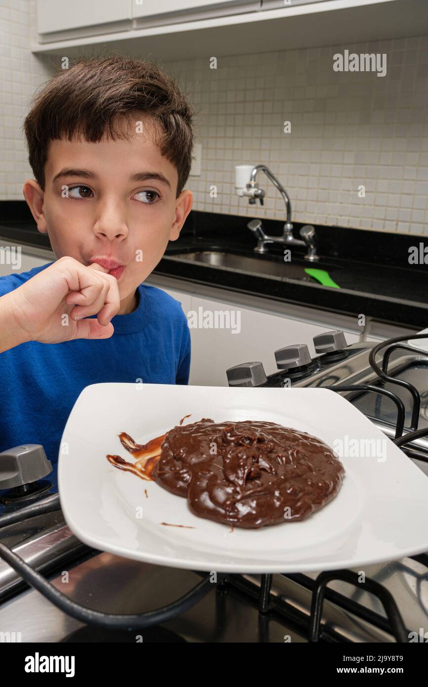 8 year old child licking his finger in front of a plate of brigadeiro. Stock Photo