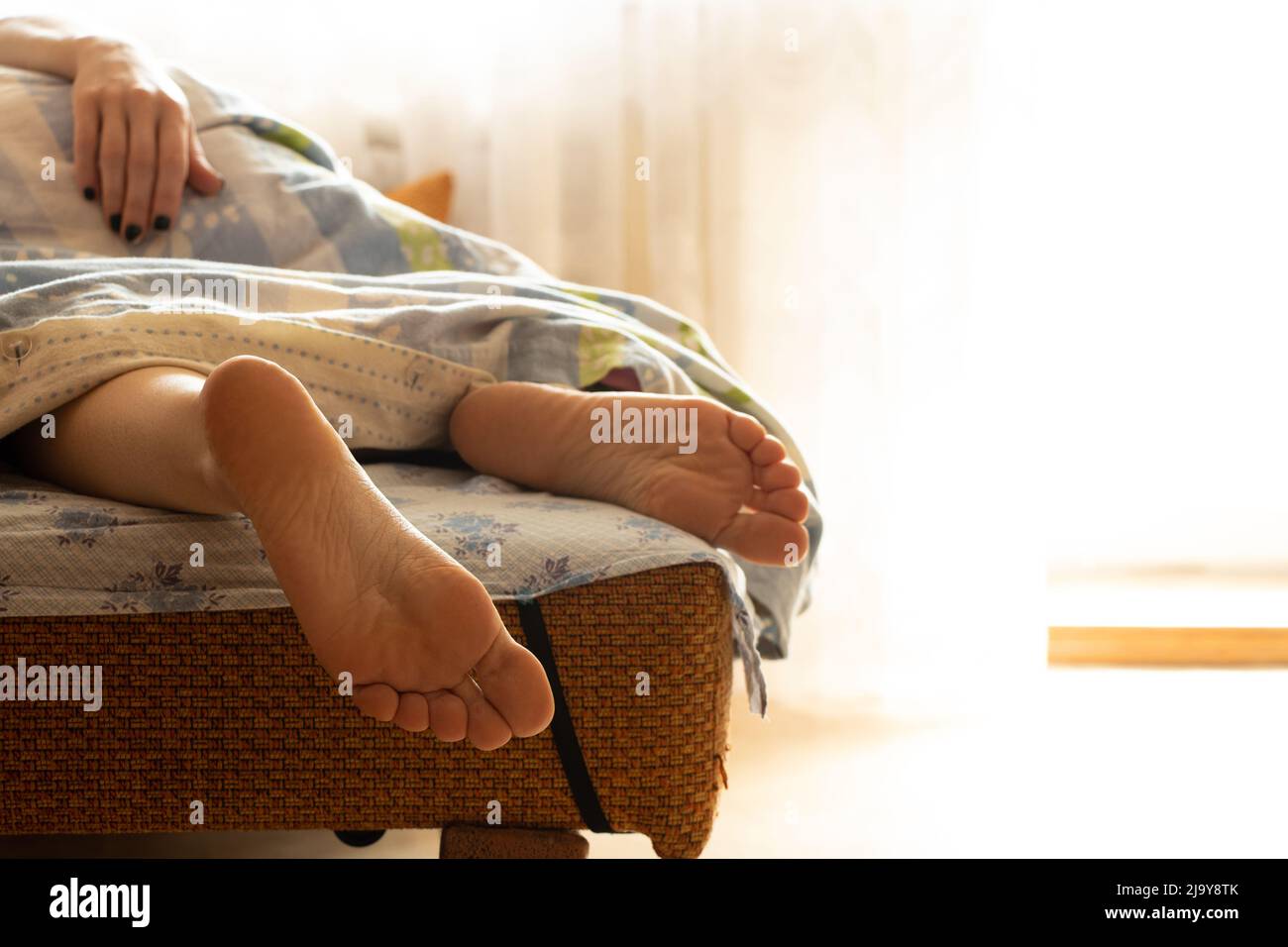 Girl's legs on the bed in a blanket at home in the morning, the girl sleeps on the bed, female legs, rest, sofa Stock Photo