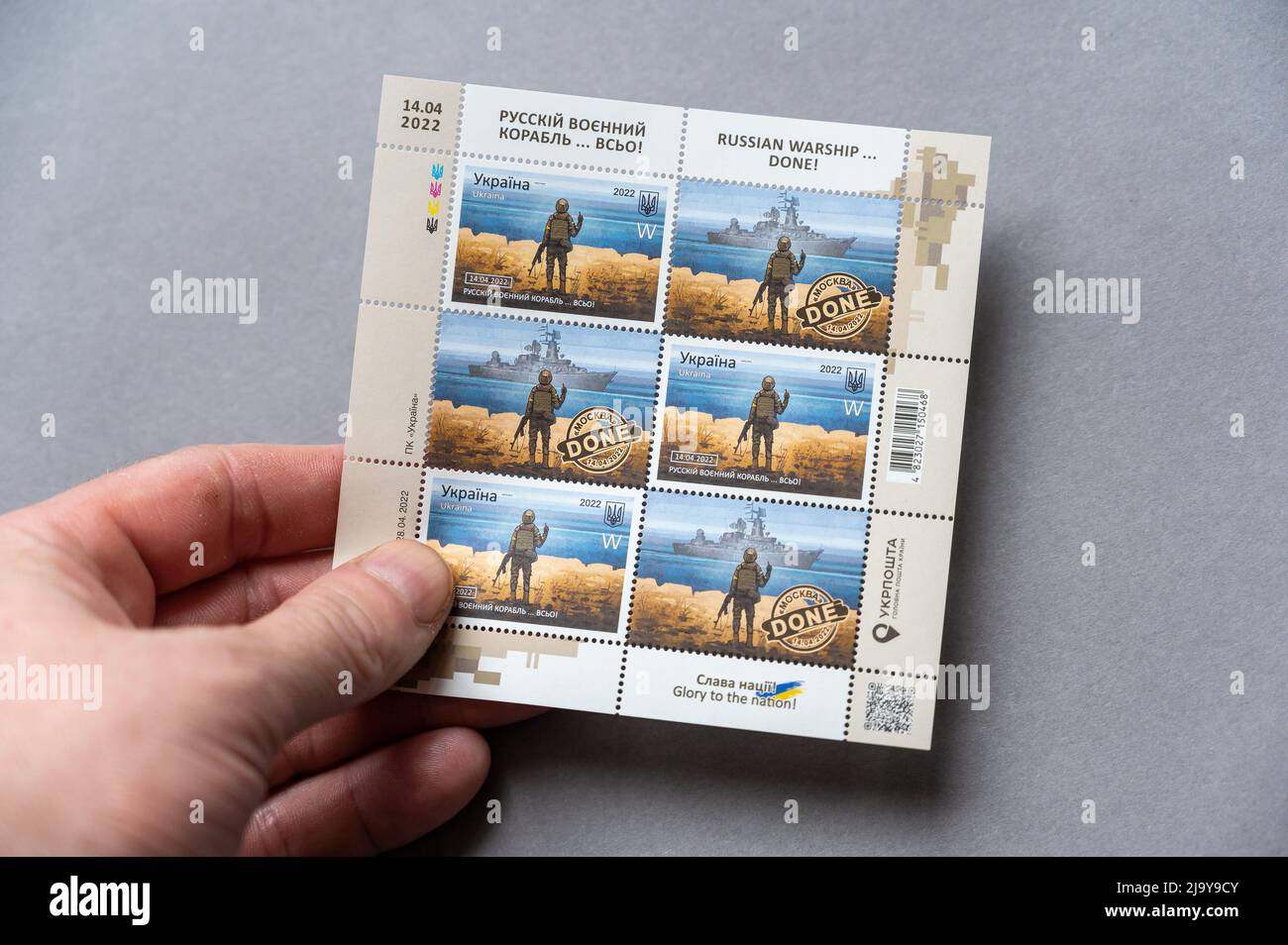 A hand holds a set of philately against a gray background. Limited edition postmarks 'Russian warship... done'. A set of postage stamps dedicated to t Stock Photo