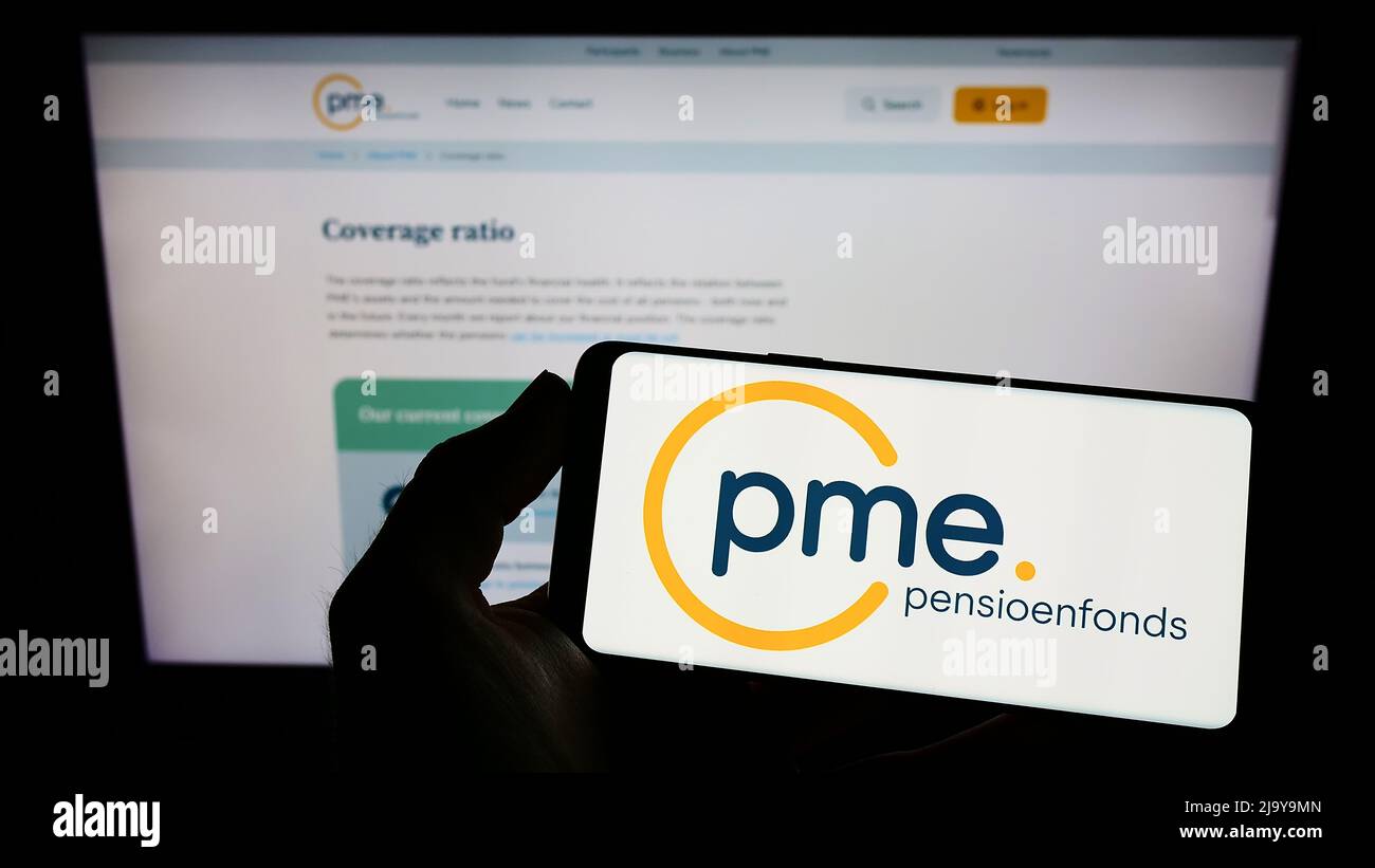 Person holding smartphone with logo of Dutch pension fund PME Pensioenfonds on screen in front of website. Focus on phone display. Stock Photo