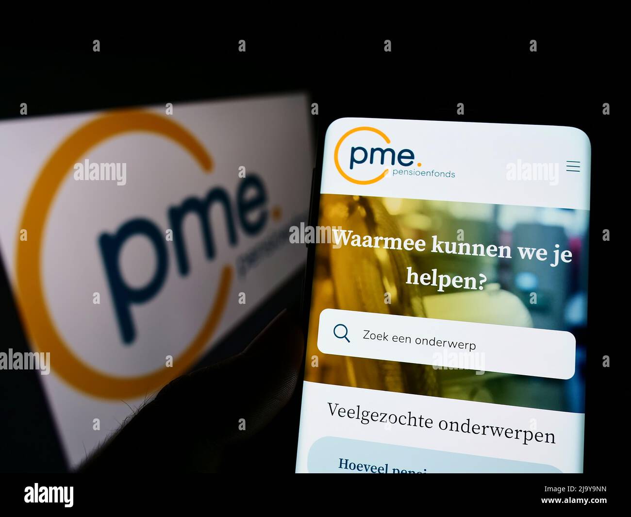 Person holding cellphone with website of Dutch pension fund PME Pensioenfonds on screen in front of logo. Focus on center of phone display. Stock Photo