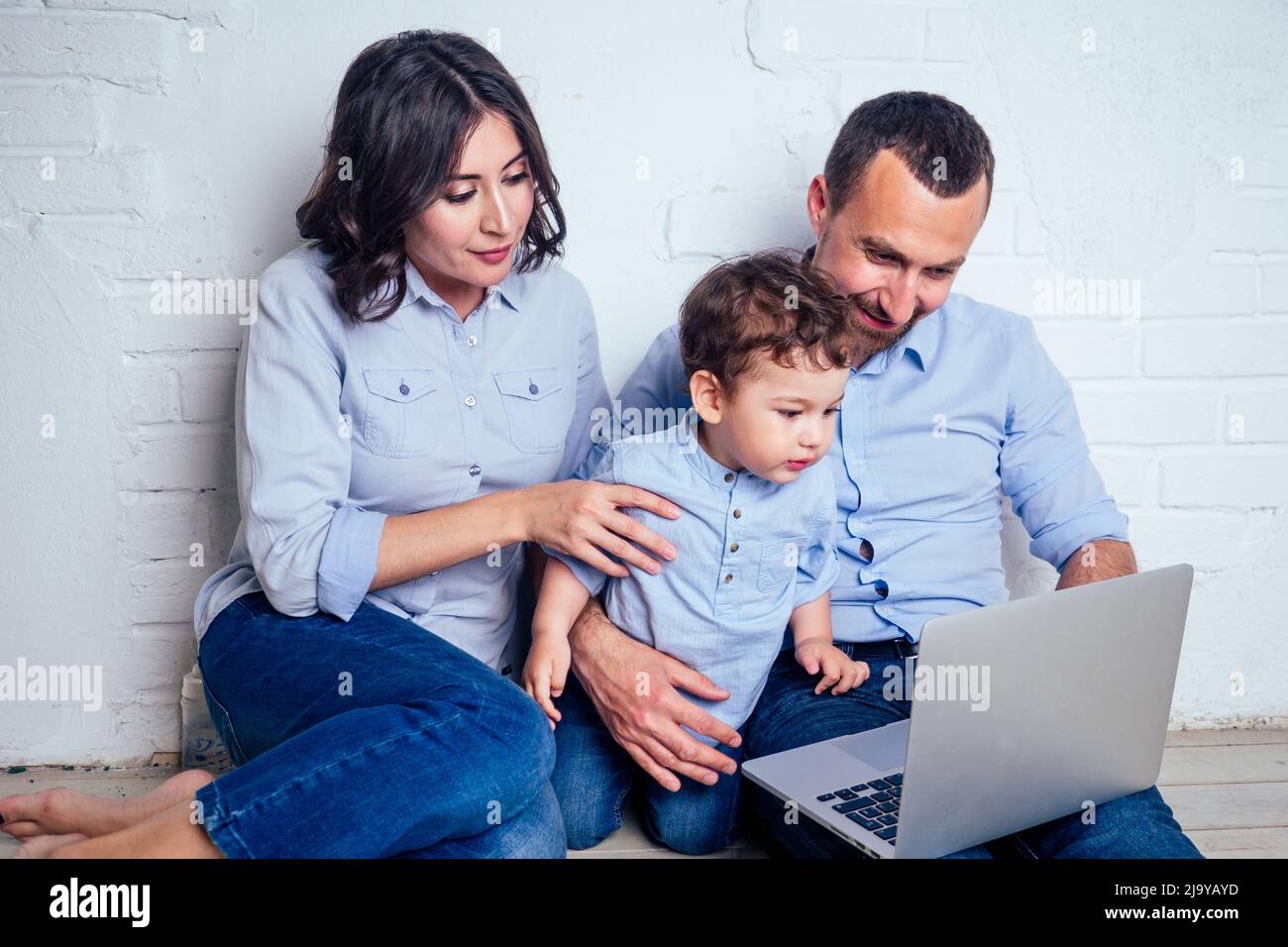 happy family beautiful mother little son and father playing developing children's game online in laptop in the apartment sitting on the floor Stock Photo