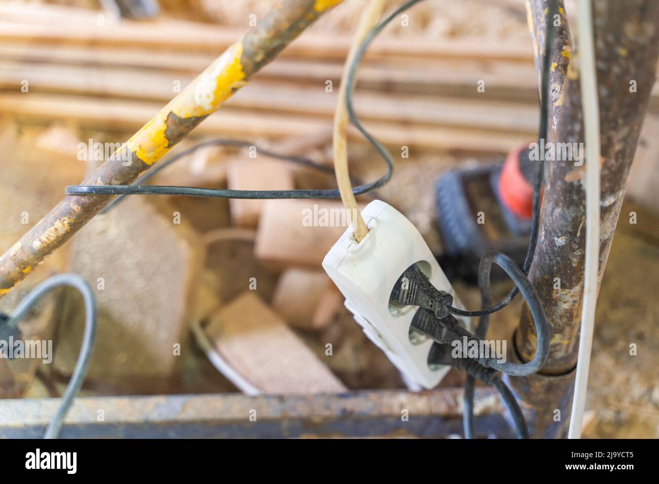 Power filter extension cord tee with euro sockets hanging on scaffolding with three connected electrical appliances, close-up Stock Photo