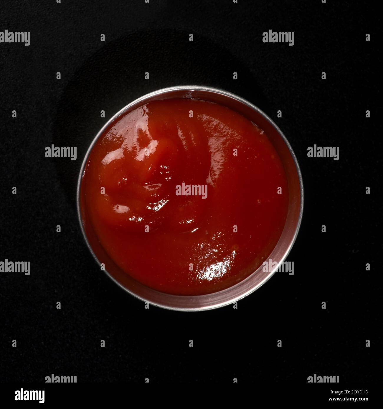 Ketchup in a metal gravy boat on a black background dope for fast food