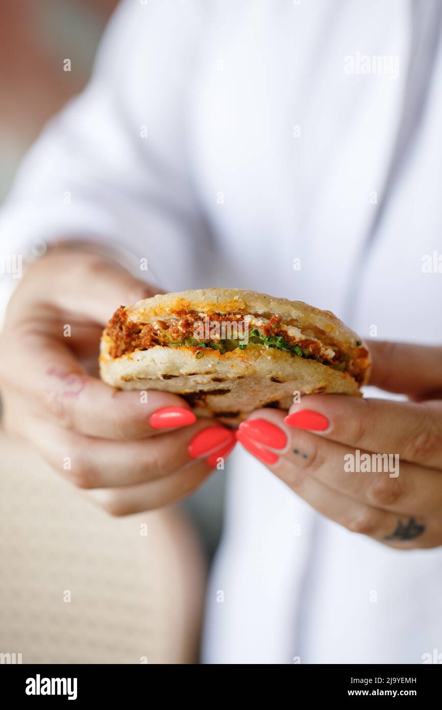 Latin girl holds an arepa in her two hands ready to eat it, Arepa stuffed with chicken Stock Photo