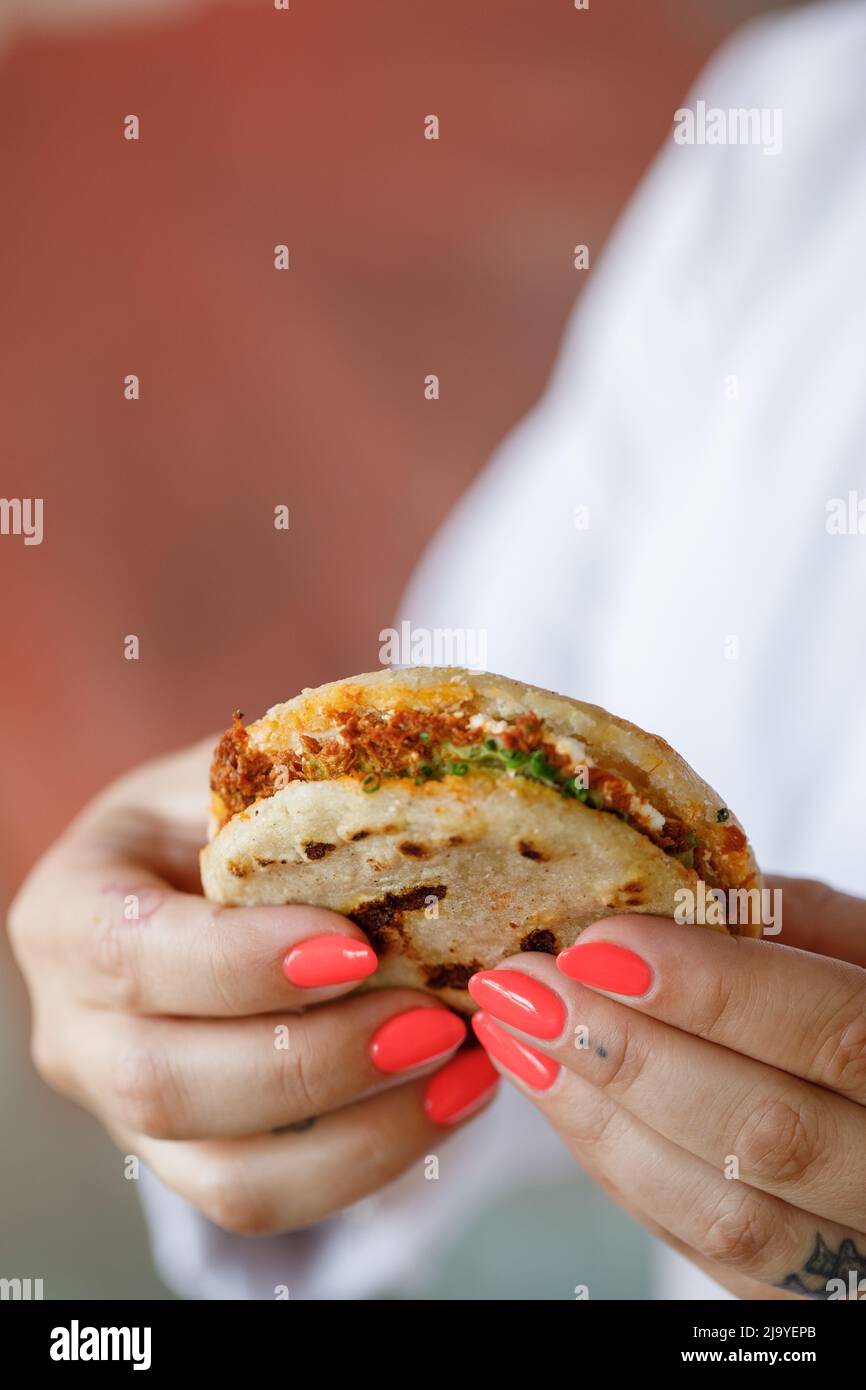 Latin girl holds an arepa in her two hands ready to eat it, Arepa stuffed with chicken Stock Photo