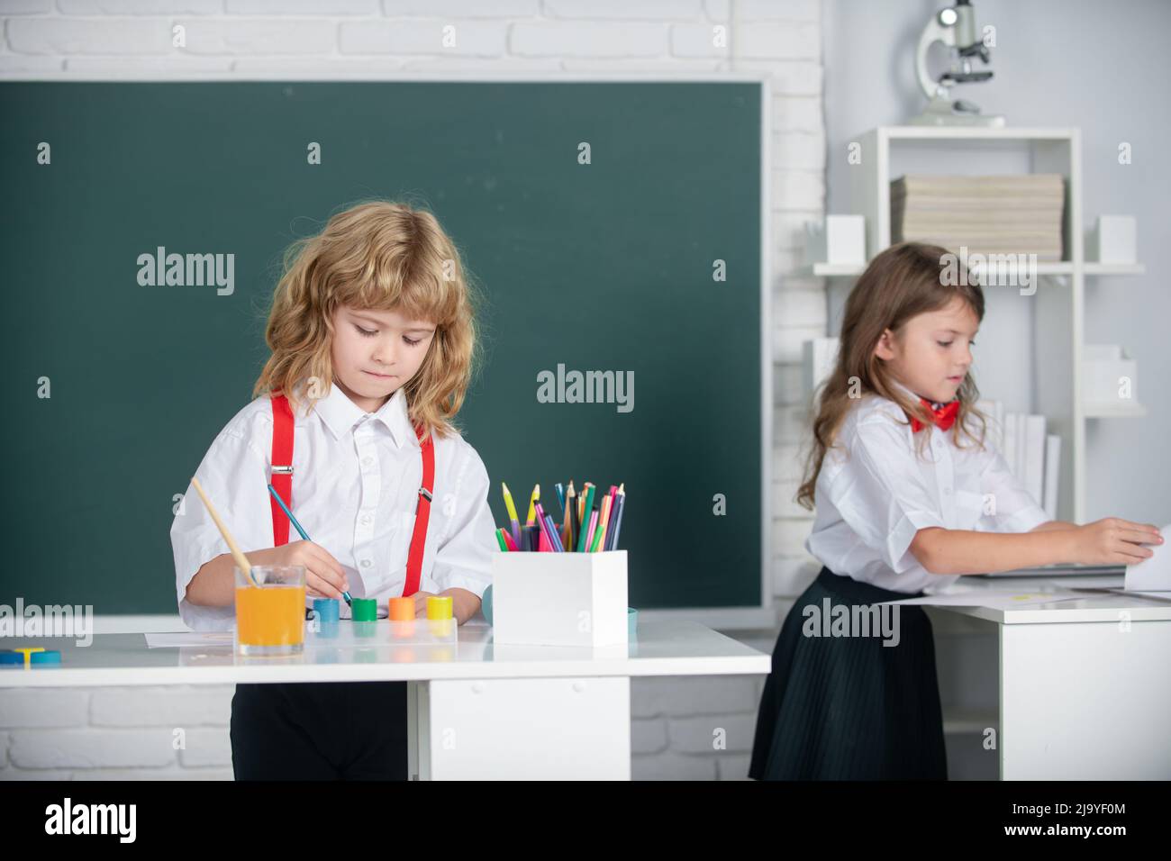 School children drawing a colorful pictures with pencil crayons in classroom. Portrait of cute pupils enjoying art and craft lesson. Cute kids draw Stock Photo