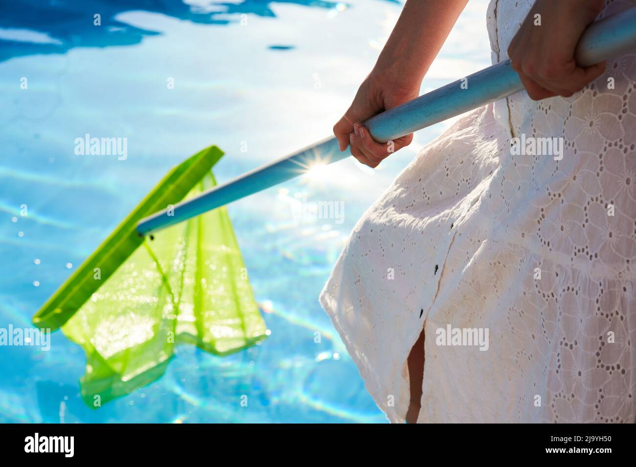 Woman with skimmer net equipment cleaning swimming pool from rubbish ...