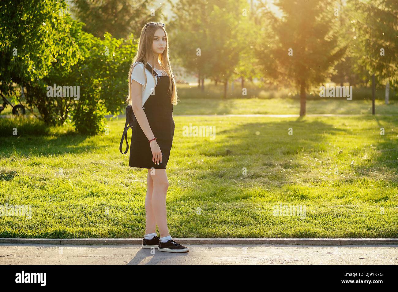 young teenager schoolgirl with long blonde hair with backpack in the park at sunset Stock Photo