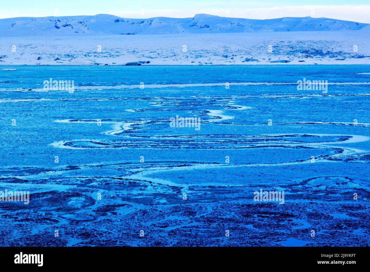 A winter 'blue hour' morning view across the Jökulsarlön iceberg lagoon with no icebergs present. The lagoon is covered by a broken layer of thin ice. Stock Photo