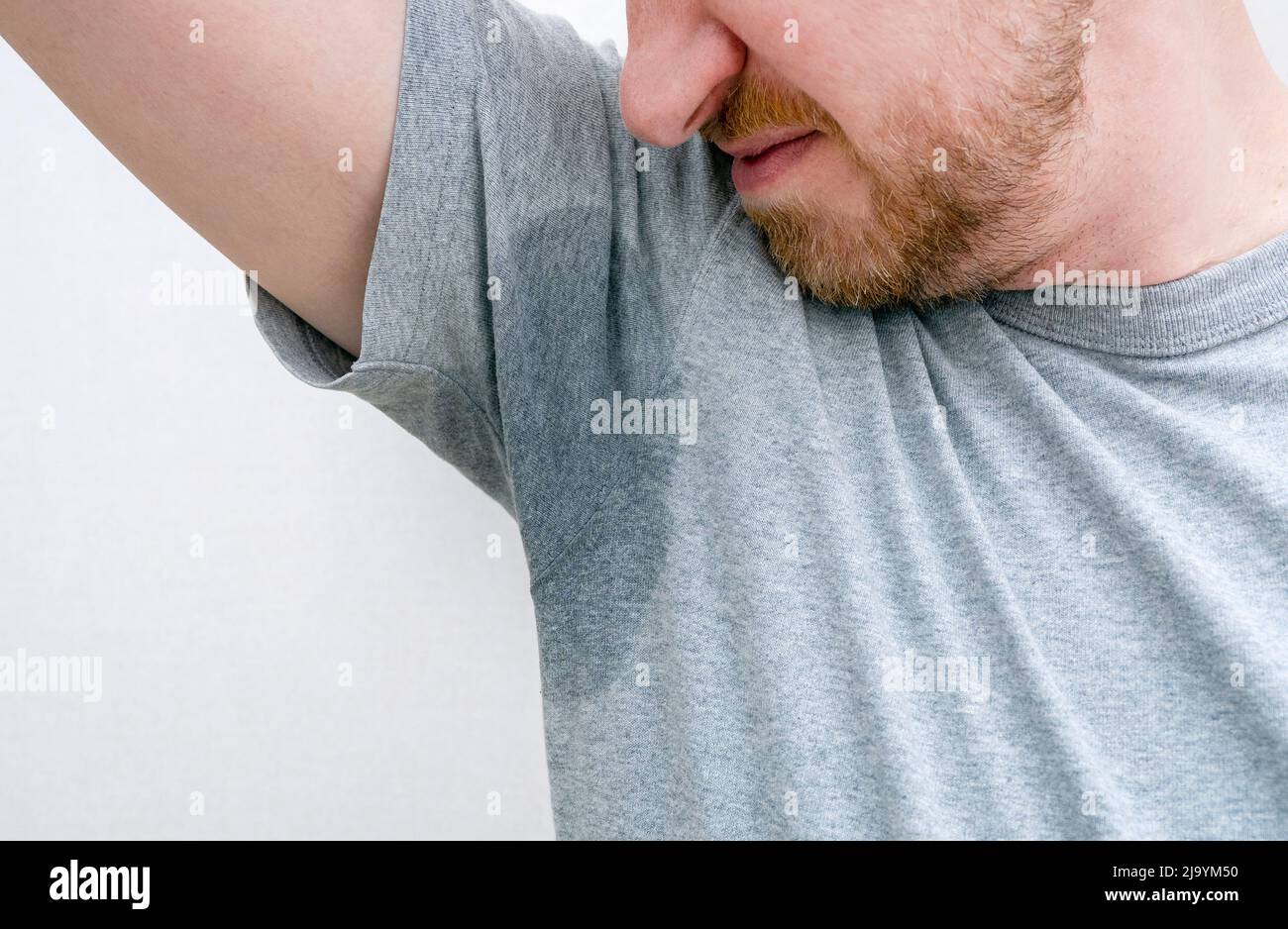 Person sniffing armpit. Sweaty armpit, wet underarm, stain of sweat on grey t-shirt Stock Photo