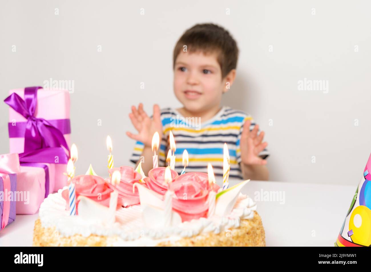 A handsome preschool boy with a cake on his birthday claps his hands on