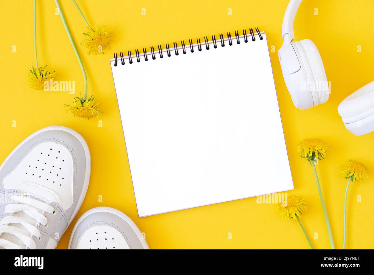 Summer template with white blank notebook, sneakers, headphones and flowers on a yellow background. Mock up in flat style. Top view. Stock Photo