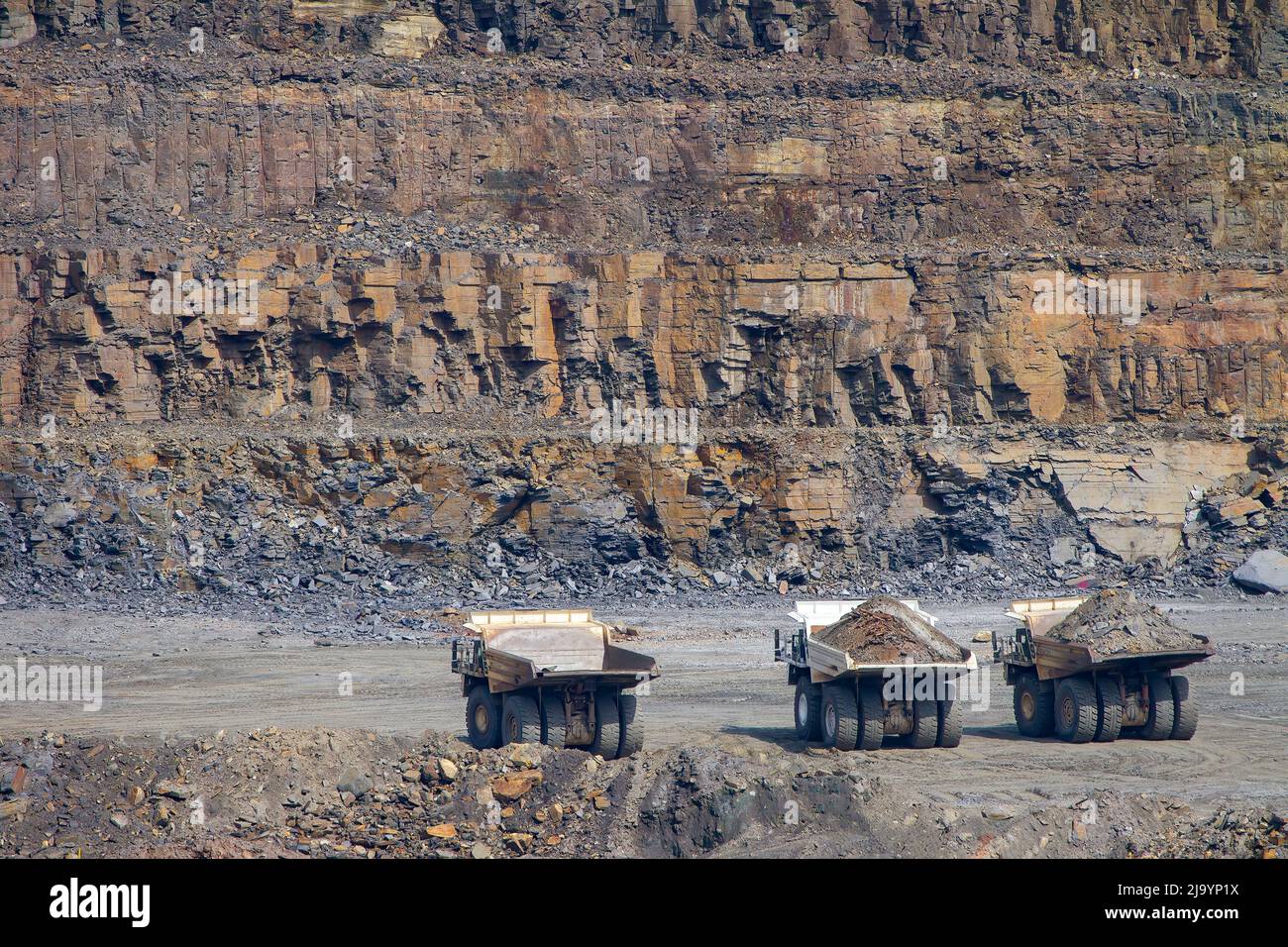 Small but Mighty: Large Haul Mining Trucks in the Vast Open Pit Stock Photo