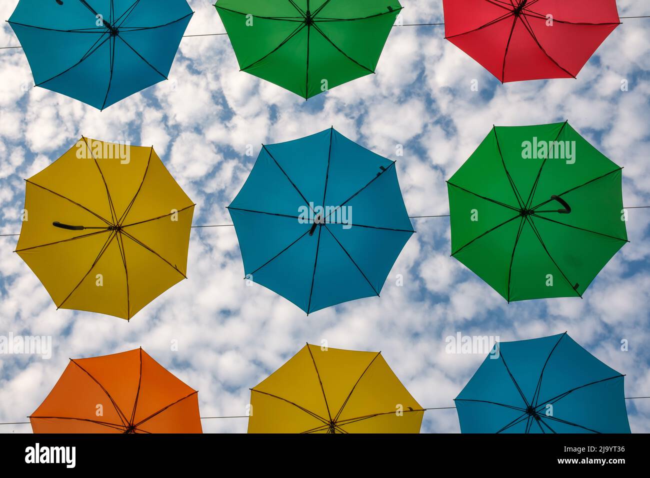 Colorful hanging umbrellas and a cloudy blue sky in the backround Stock Photo