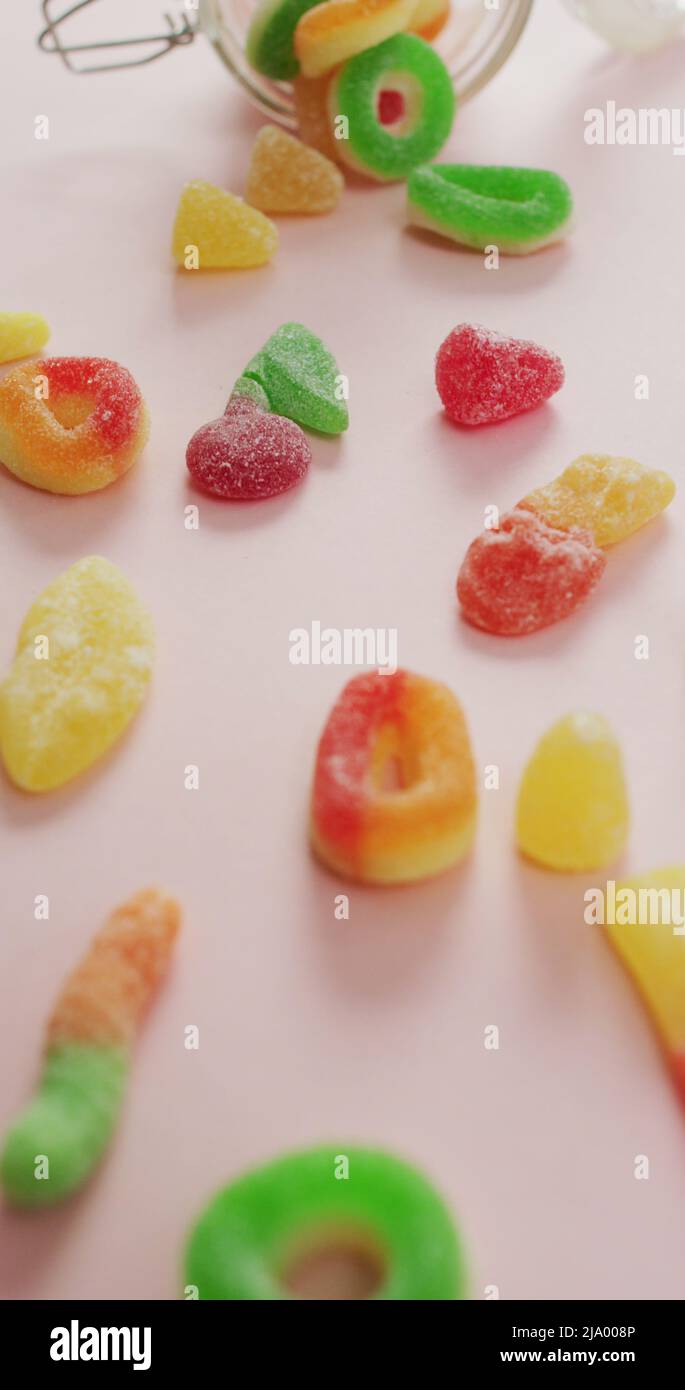Vertical image of jelly candy spilling out of glass jar on pink background Stock Photo Alamy