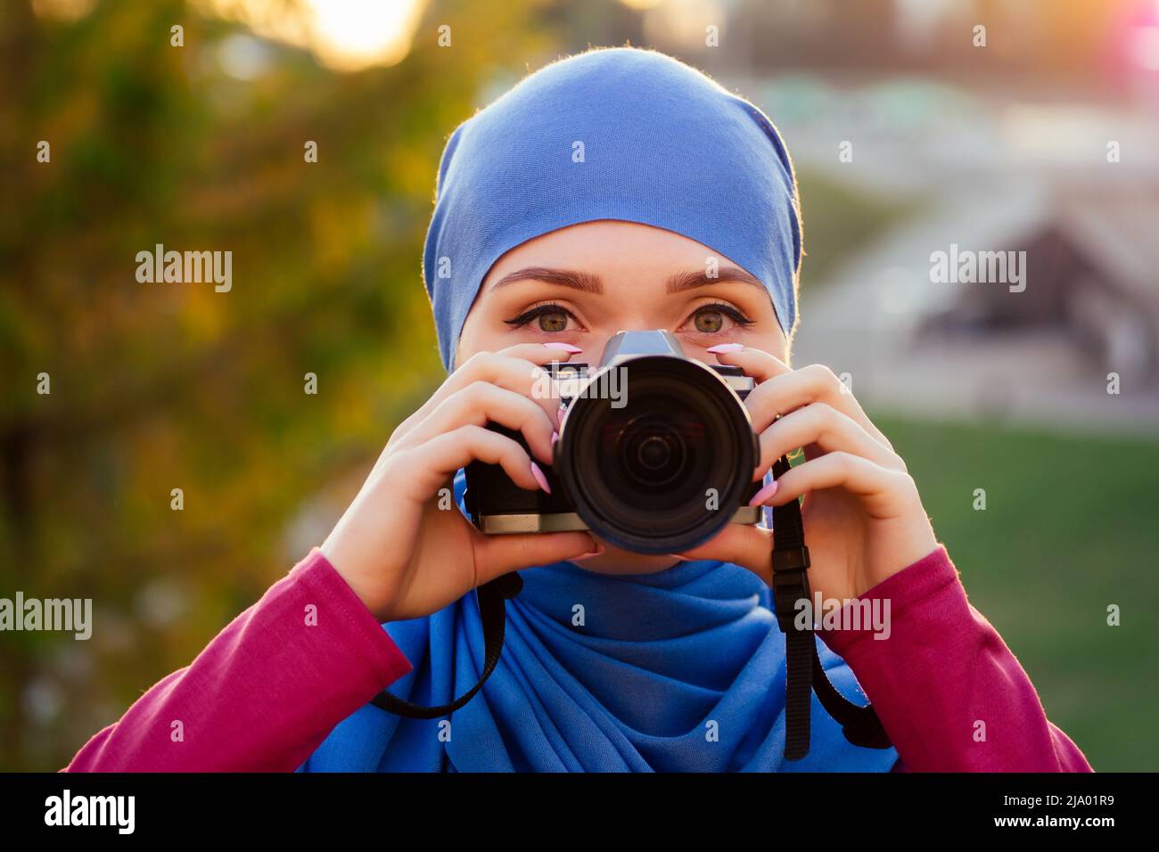 Female photographer wearing a hijab. woman holding a camera hobbyist or a journalist in summer park autumn trees forest Stock Photo