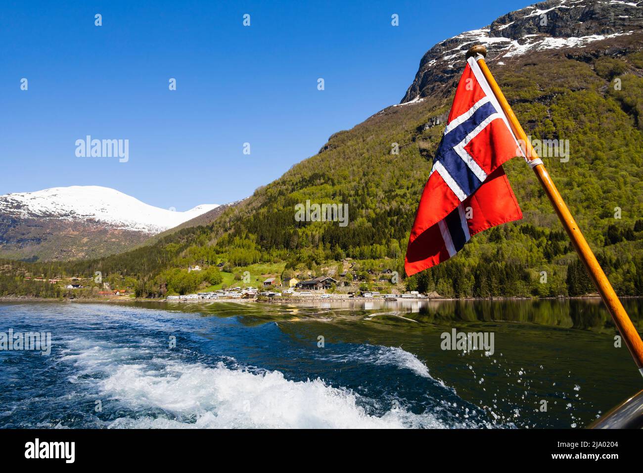 Norwegian flag flying on a boat cruising down Lake Lovatnet, Norway Stock Photo