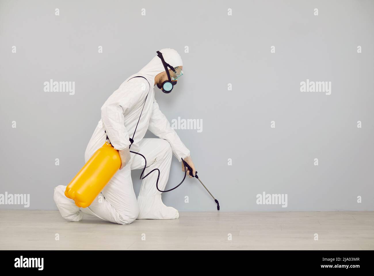 Pest control worker in protective suit spraying insecticide to clean