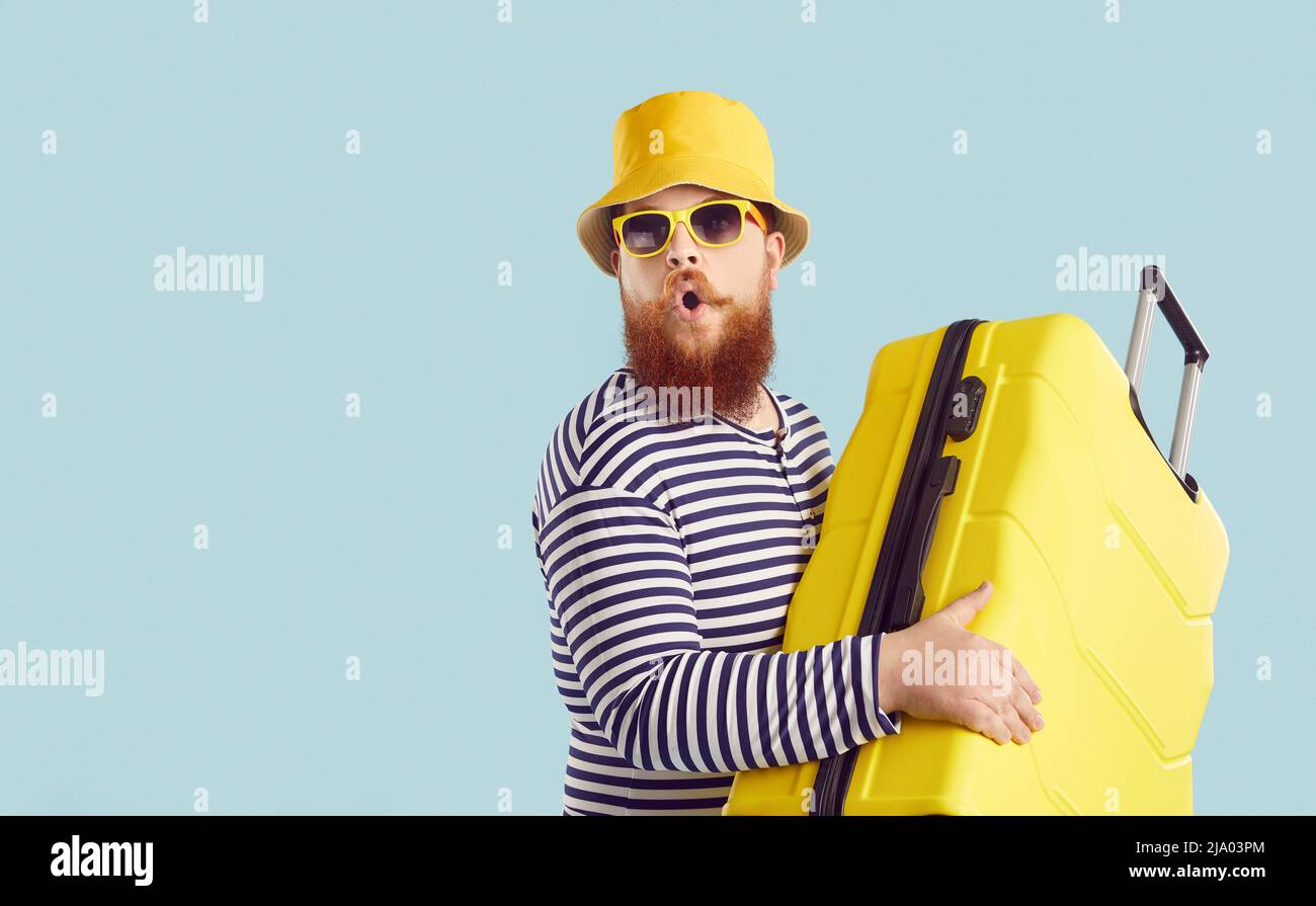 Funny surprised man in hat, sunglasses and swimsuit going on holiday with his yellow suitcase Stock Photo