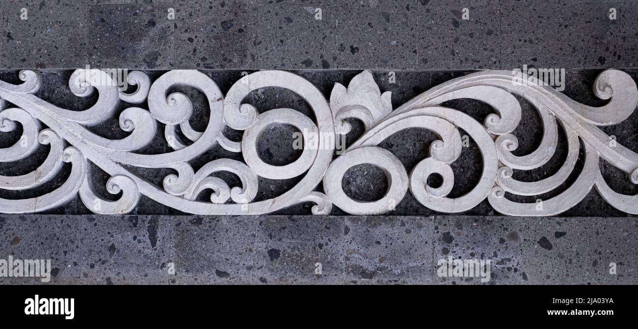 White intricate cement scrolled architectural design element in between gray stone wall section Stock Photo