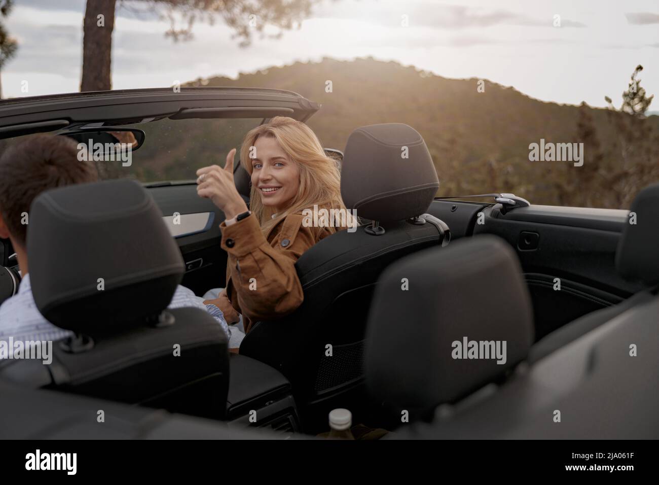 Pretty happy young woman showing thumb up and smiling sitting in cabriolet car with her man Stock Photo