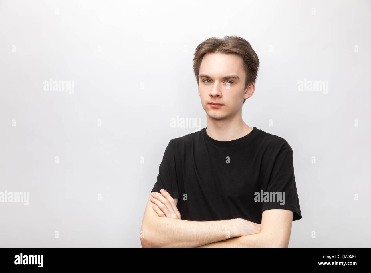 Portrait of suspicious young man wearing black tshirt holding his hands crossed looking at camera. Studio shot on gray background Stock Photo