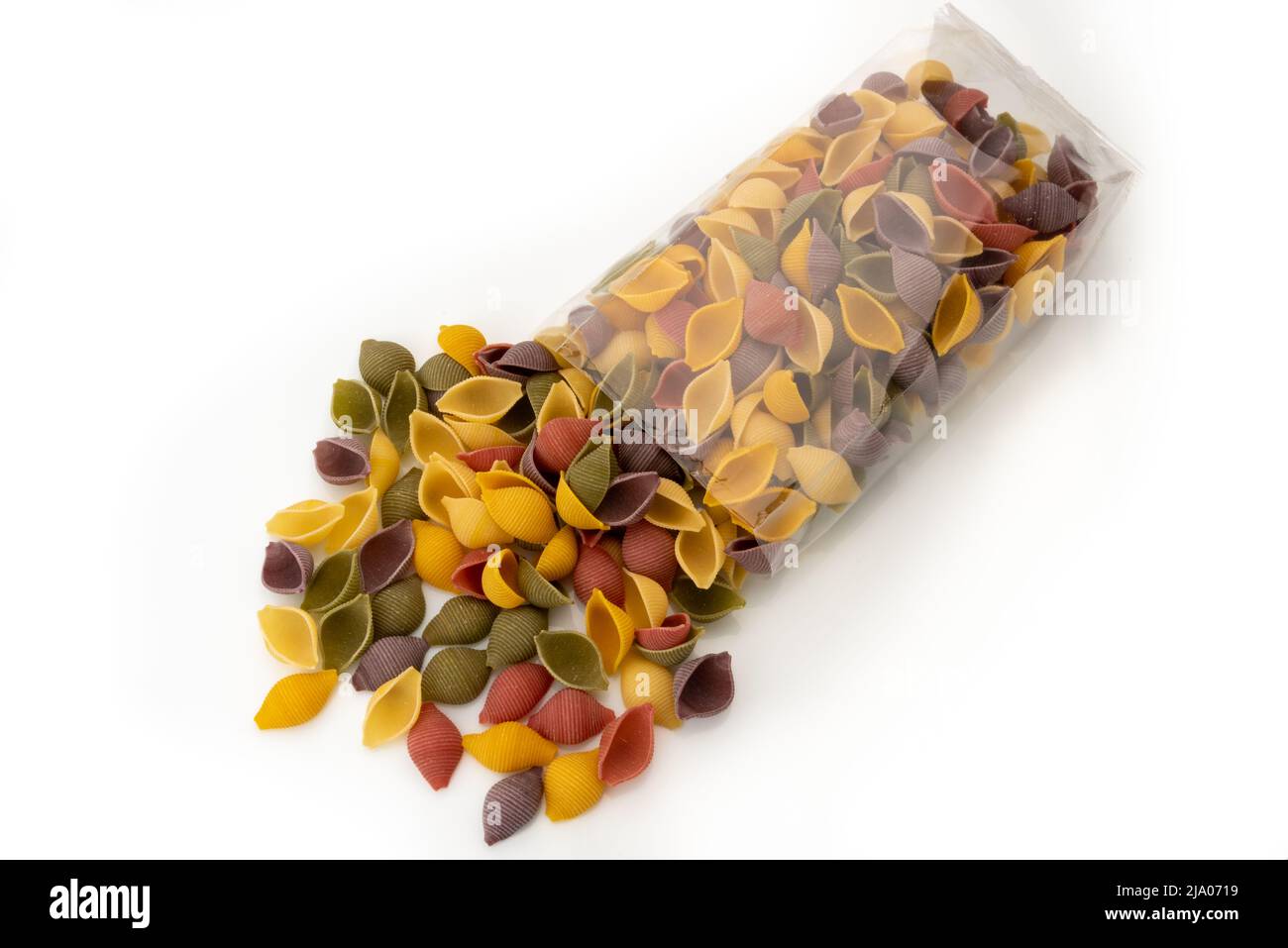 Colored pasta conchigle (shells) that come out of transparent bag, italian durum wheat semolina pasta with turmeric, spinach, beetroot and black carro Stock Photo