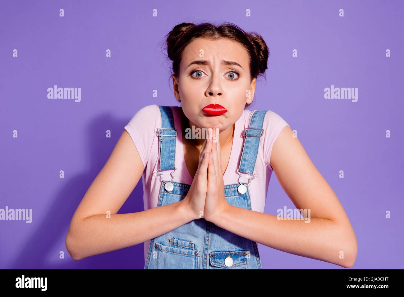 Portrait of pretty pleading begging person pouted lips hands palms together isolated on purple color background Stock Photo