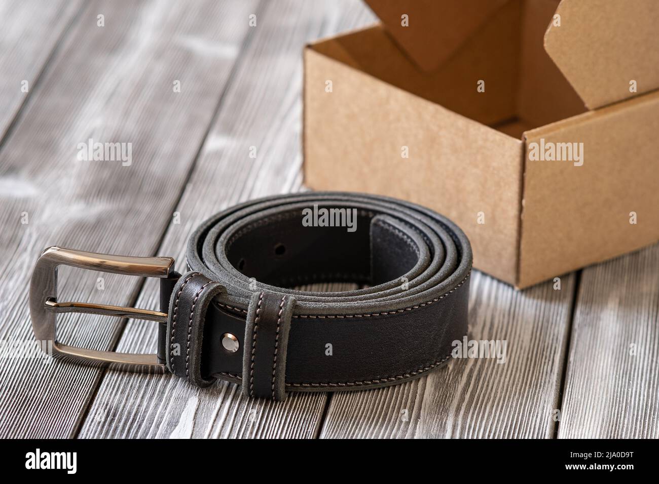 Stylish belt made of black leather and steel fittings on a wooden background. An expensive gift option for men, women, premium leather, a chic surpris Stock Photo