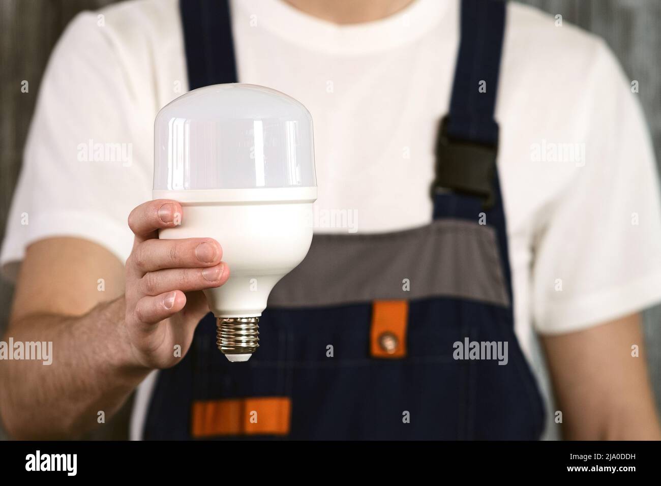 An electrician in overalls holding an energy-saving light bulb in his hands. Stock Photo