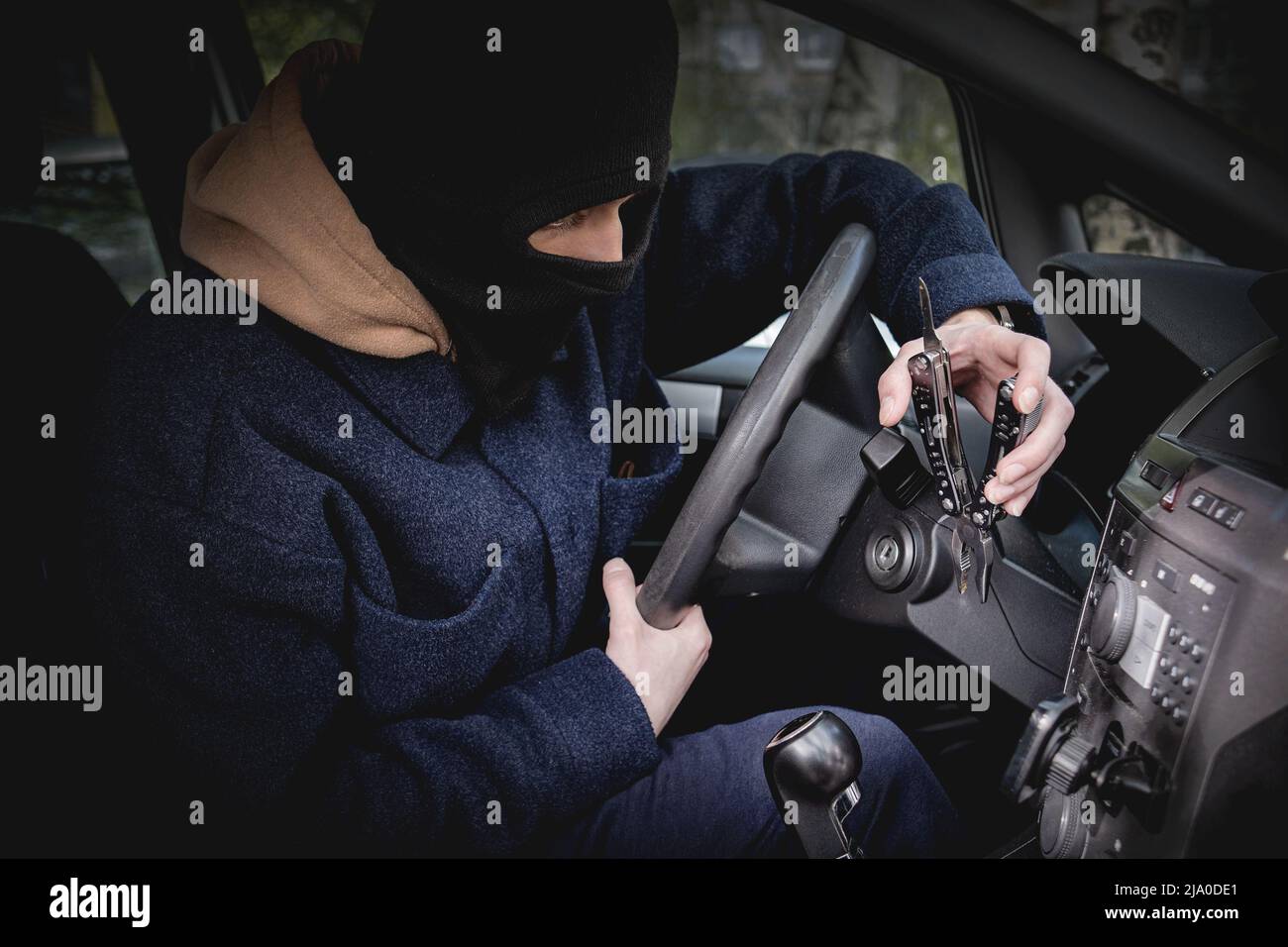 A car thief in a mask excluding recognition, tries to open the ignition lock with a tool. Crime, car theft Stock Photo