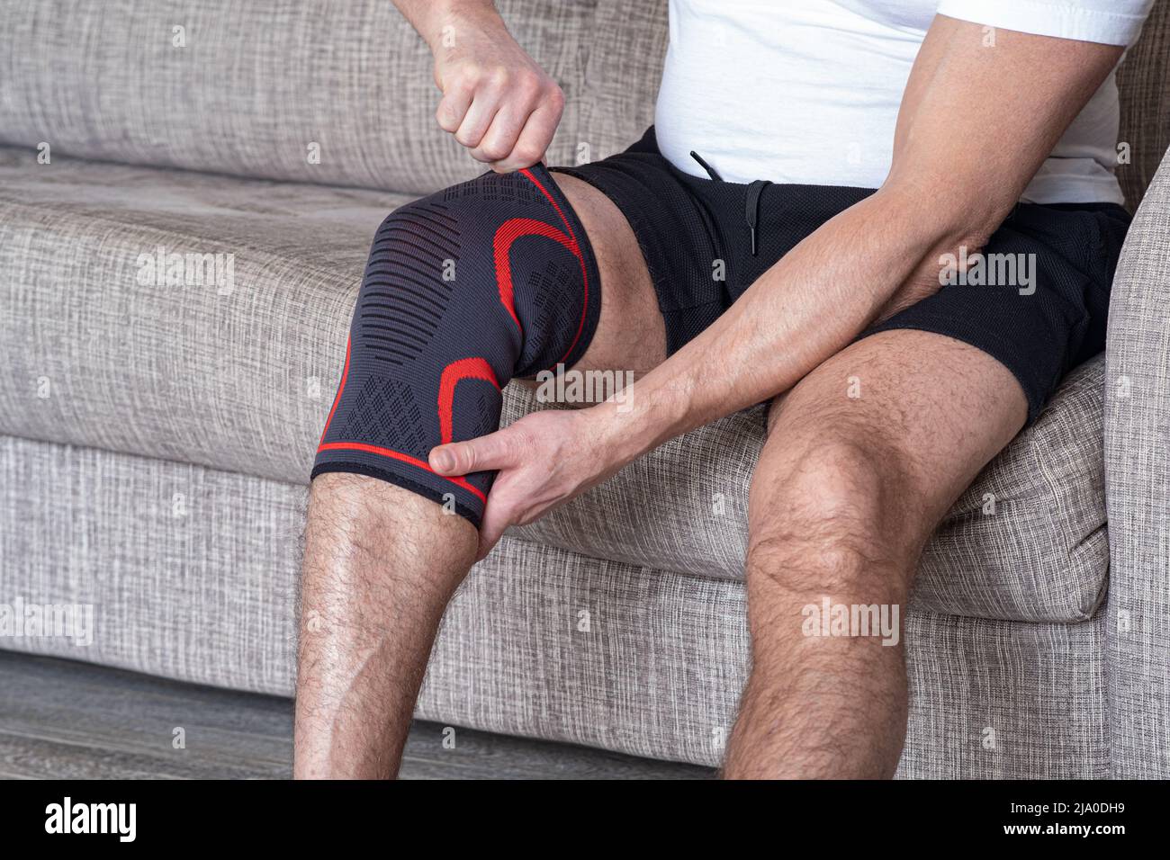 The guy puts a compression bandage on the injured knee. Preparing for sports activities, the sore spot is highlighted in red Stock Photo