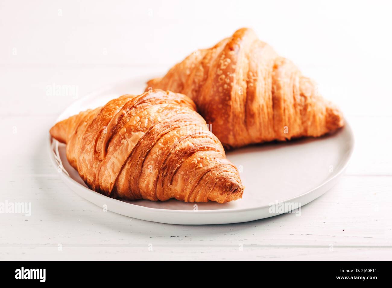 Plate with two fresh croissants on white table. Stock Photo