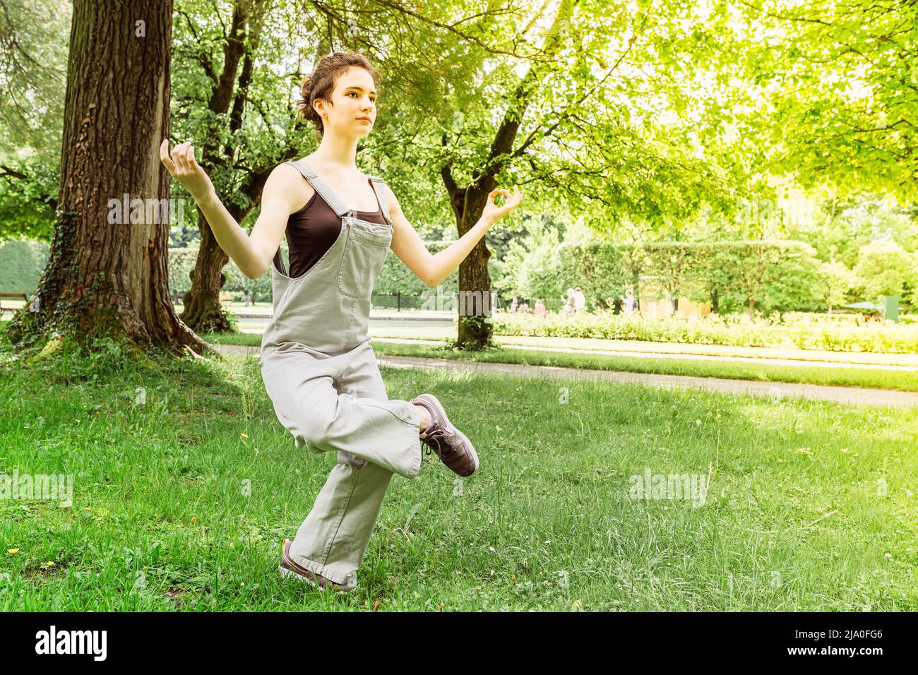 Teenage girl with open eyes practicing yoga in park, Yoga Natarajasana, Lord of Dance, balancing on one leg, hands in namaste. unity with nature Stock Photo