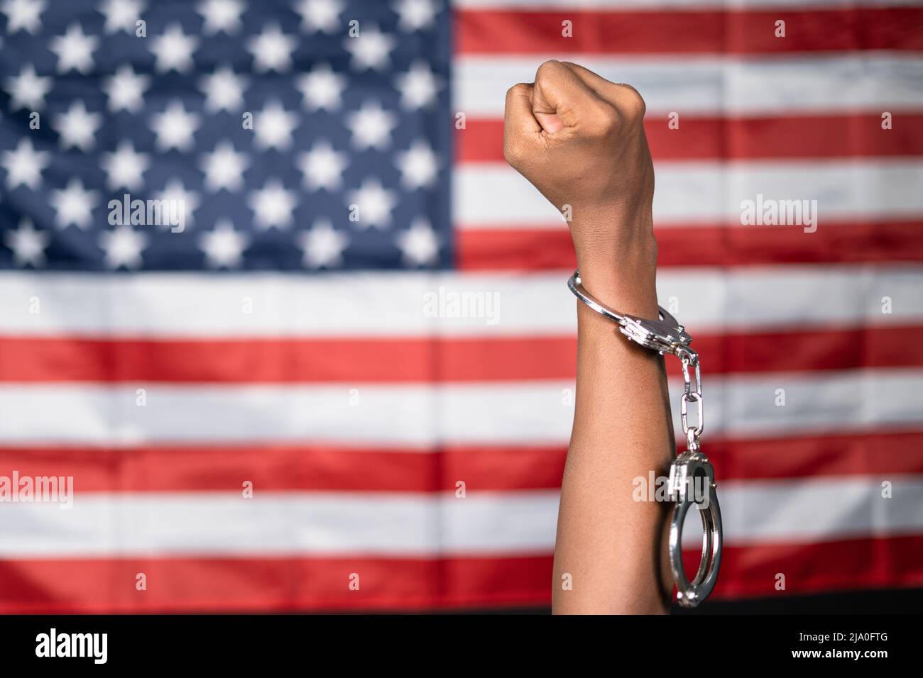 Close up shot of hanads rising with cuffs against us or american flag - concept of juneteenth, freedom and punishment. Stock Photo